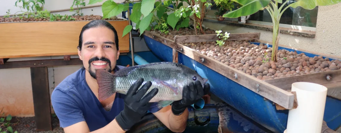 Leandro Laureti, do Aquaponia MS, com uma tilápia ao lado do sistema de aquaponia