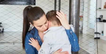 Mãe acolhendo o filho no colo em casa, cena do dia a dia de uma família atípica